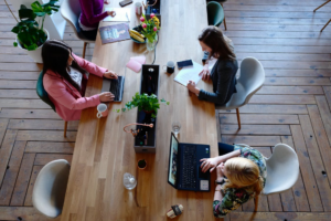 Three women sitting on white chairs in front of a table.